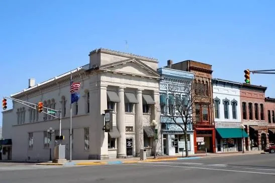 A historic downtown street corner in Plymouth, Indiana, lined with early-1900s storefronts and civic buildings under a clear blue sky.